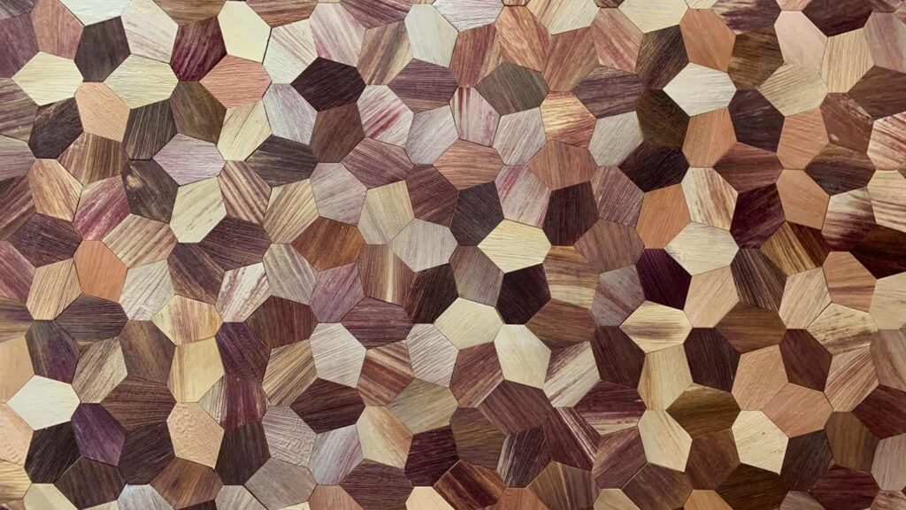 A hexagonal wood pattern featuring various shades of brown, beige, and cream. The pieces are arranged in a geometric design, creating a textured surface.