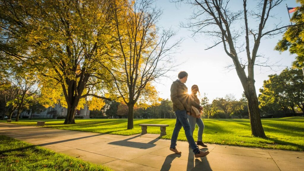 Two people walk in a greenspace with the sun behind them
